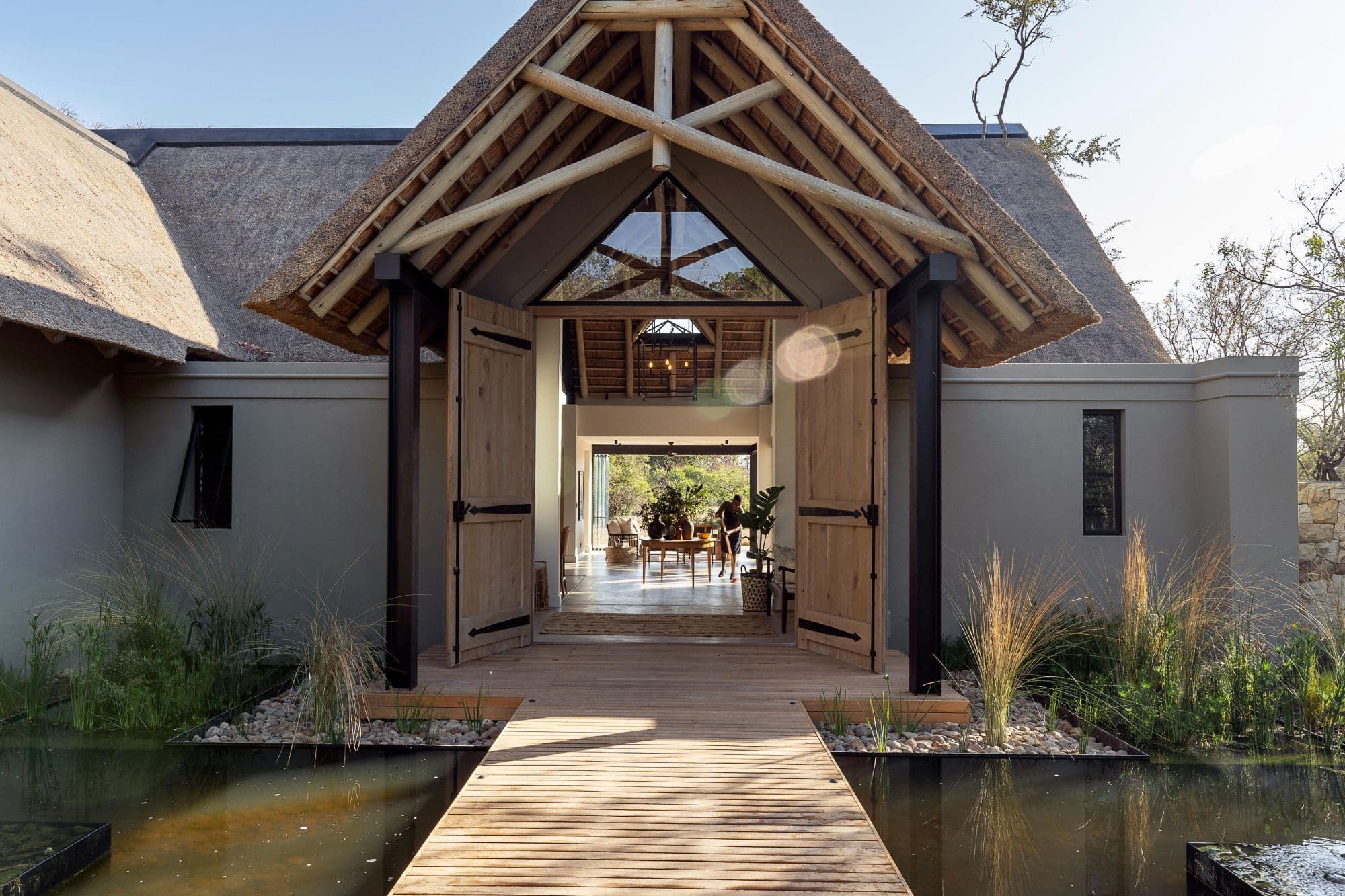 The lodge entrance — thatched gable, timber doors and a walkway between lily ponds