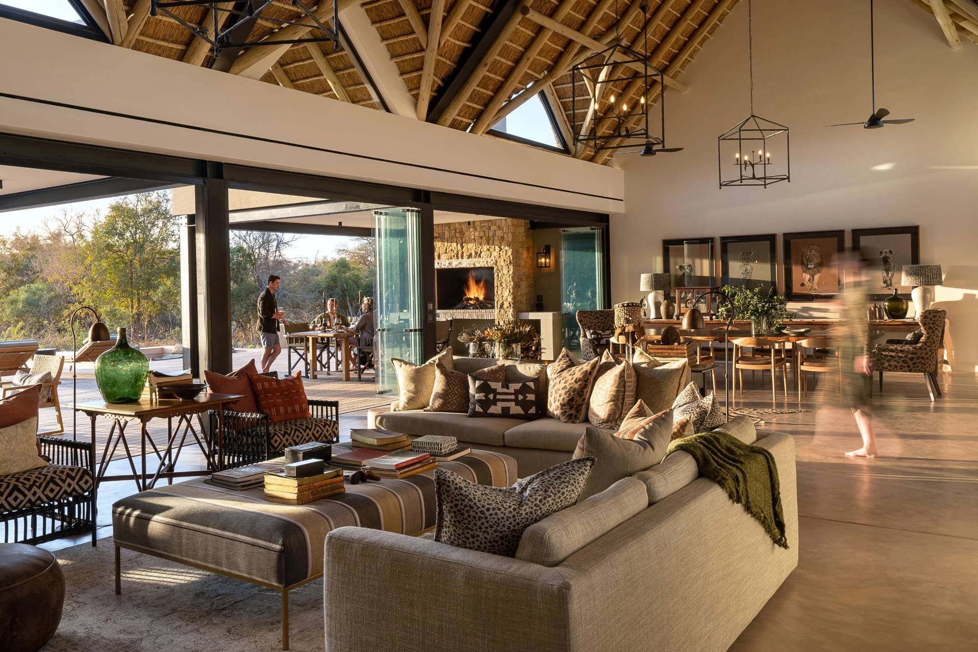 The main lodge lounge — open-plan, stone fireplace, doors folded back to the bush
